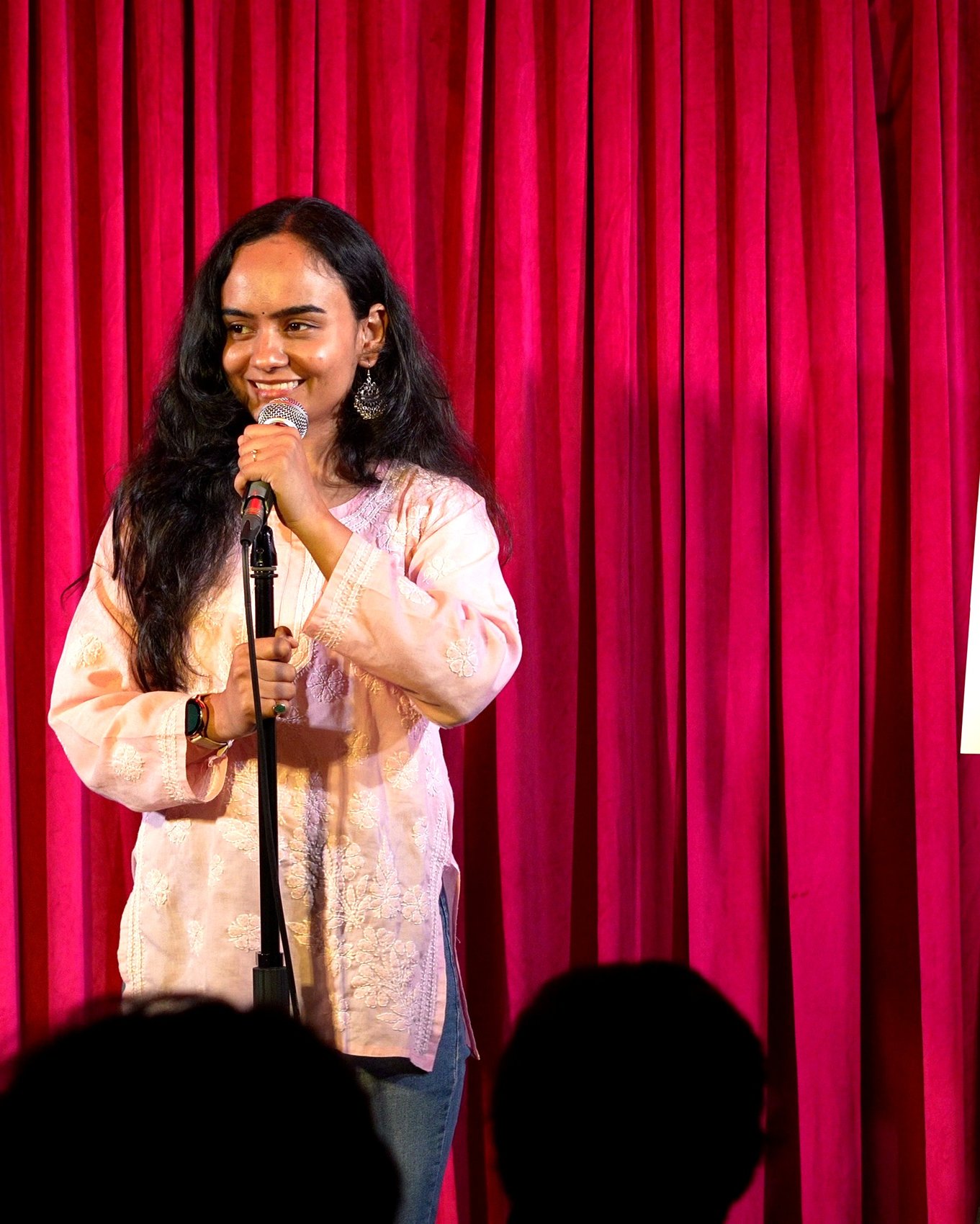 Performer smiling on stage at Tarang open mic